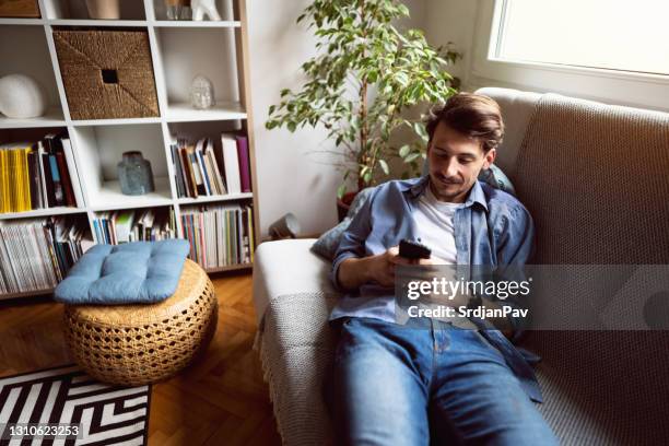 young man relaxing on the sofa at home - stress free life mobile stock pictures, royalty-free photos & images