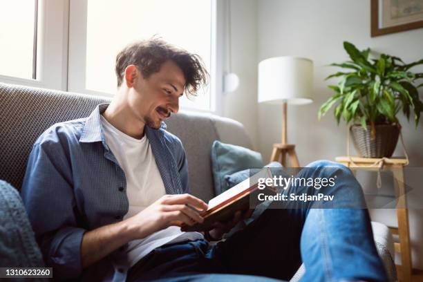 young man reading a book at home - reading stock pictures, royalty-free photos & images