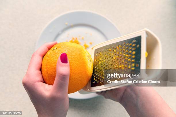 zesting an orange using a metal grater, - grater stock pictures, royalty-free photos & images