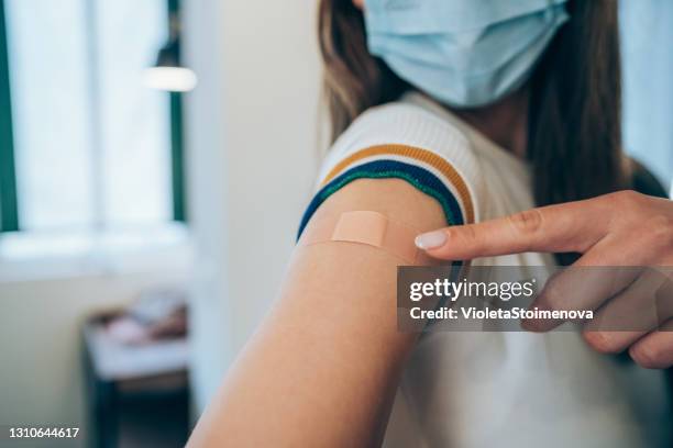 woman showing her arm after getting vaccinated. - influenza vaccination stock pictures, royalty-free photos & images