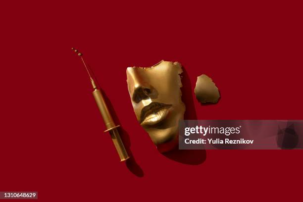 gold colored syringe and face/ mask on the red background. - chirurgia plastica foto e immagini stock