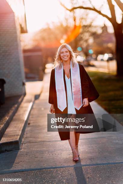 portrait of a happy college university graduate walking and wearing a pink sash - maroon graduation stock pictures, royalty-free photos & images