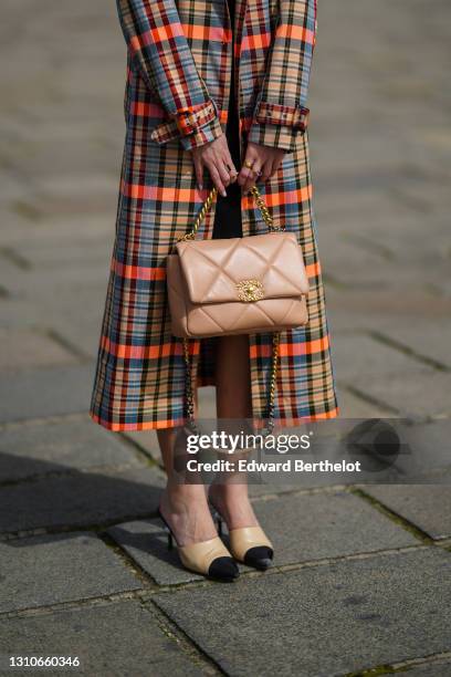 Alba Garavito Torre wears a neon orange and blue colored checked trench coat from Munthe, a beige leather quilted Chanel bag, Chanel slingback shoes...