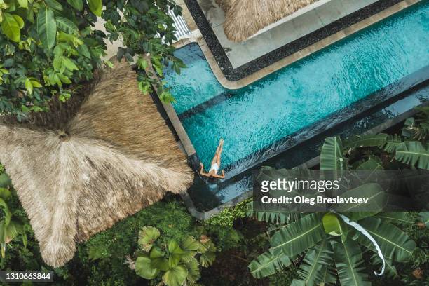 woman enjoying alone in luxury swimming pool, drone view from above - tropical climate stock-fotos und bilder