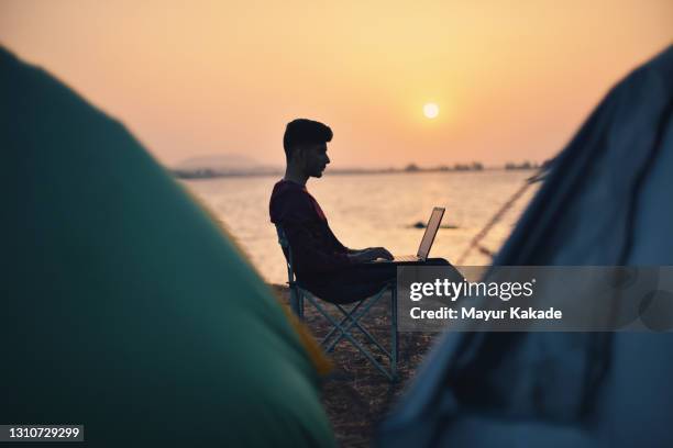 young man working on laptop sitting near a serene lake during sunset - millennial generation at work stock pictures, royalty-free photos & images