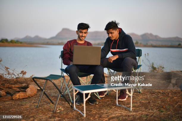 two young men working on laptop outdoors at the bank of a serene lake - camping chair stock pictures, royalty-free photos & images