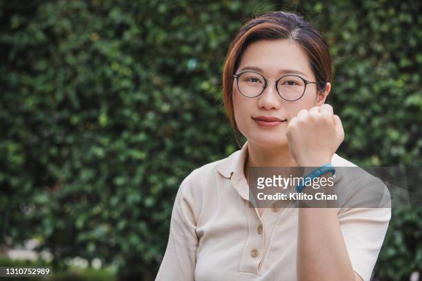portrait of asian woman holding a fist with hand wearing "covid-19 vaccinated" rubber wristband - rubber bracelet stock pictures, royalty-free photos & images