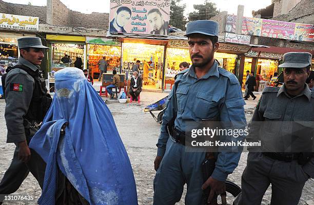 Woman in blue burka passes by policemen standing at a check point in a busy market place in Deh Afghanan on October 15, 2011 in Kabul, Afghanistan.