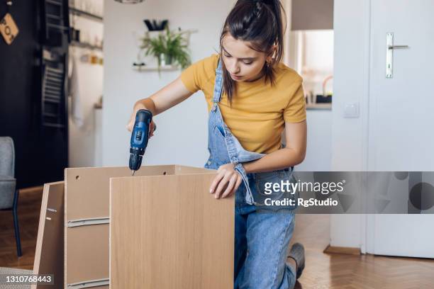 portrait of a girl working with electric screwdriver and making a wooden shelf - electric screwdriver stock pictures, royalty-free photos & images