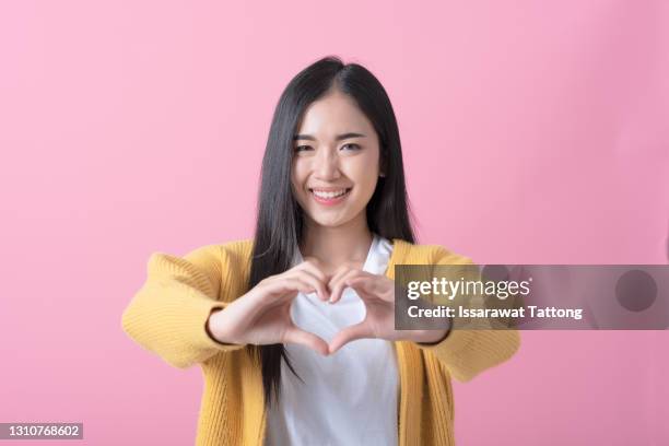 pretty romantic young woman making a heart gesture with her fingers in front of her chest showing her love and affection with a happy tender smile - young at heart ストックフォトと画像