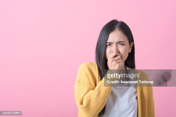 bright young woman covers his nose due to bad smell  isolated on pink background - offensive stockfoto's en -beelden