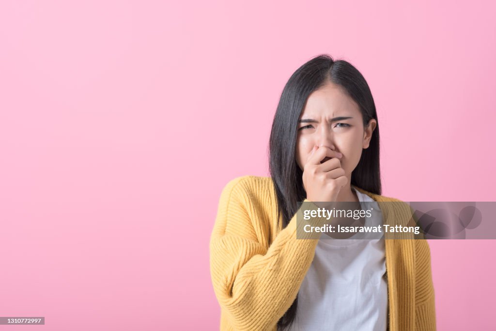 Bright young woman covers his nose due to bad smell isolated on pink background