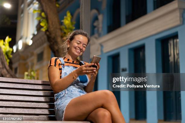 mulher em chamada de vídeo sentada no banco quadrado - praça - fotografias e filmes do acervo