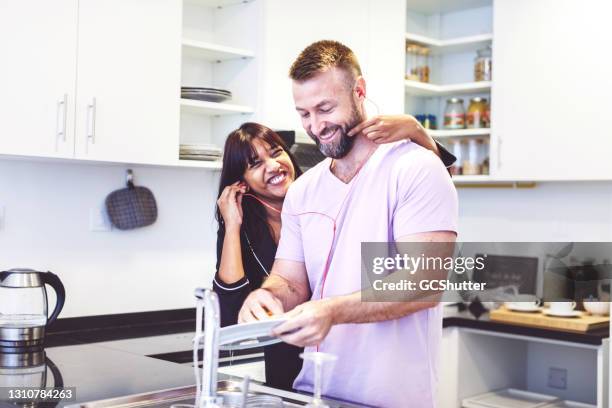 wife teasing her hushabd while he is cleaning the dishes - expatriate stock pictures, royalty-free photos & images