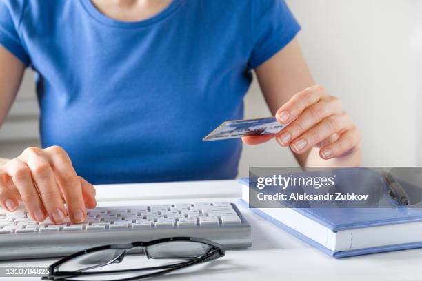 the woman is holding a credit card, typing on a laptop keyboard, entering personal data. next to the notebook and pen, glasses. the concept of buying online, ordering goods at home and paying via the internet. - datos personales fotografías e imágenes de stock