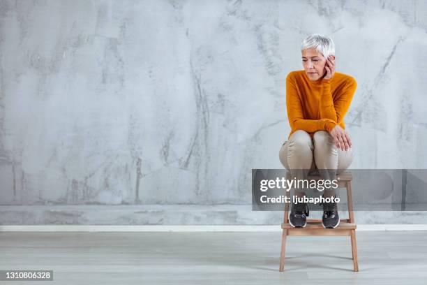 beautiful dreamy mature woman with grey hair sitting on chair isolated on grey - woman full length studio stock pictures, royalty-free photos & images