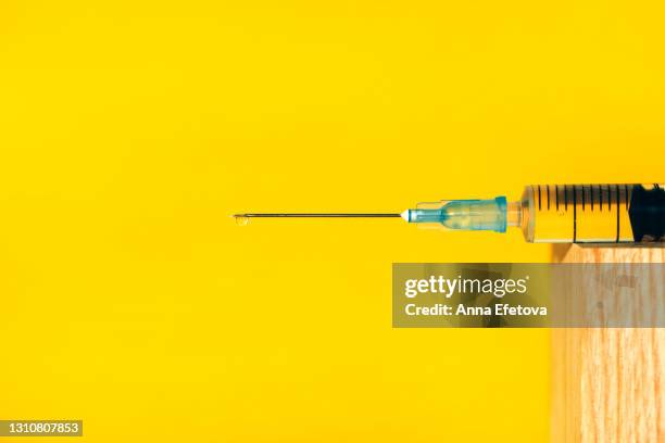 disposable plastic syringe with drop of fluid medication on needle placed on wooden podium against illuminating yellow background. vaccination is the most anticipated procedure of the year 2020 and 2021. trendy colors of the year. close-up and front view - job aids stock pictures, royalty-free photos & images