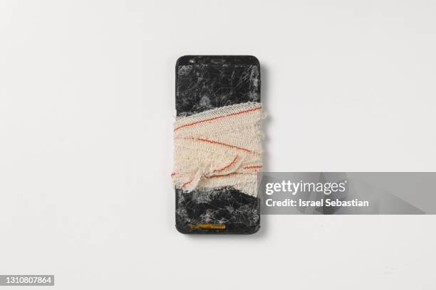 top view of a mobile phone with a broken screen because it has fallen to the ground. the cell phone is wrapped with a medical bandage. - screen replacement stock pictures, royalty-free photos & images