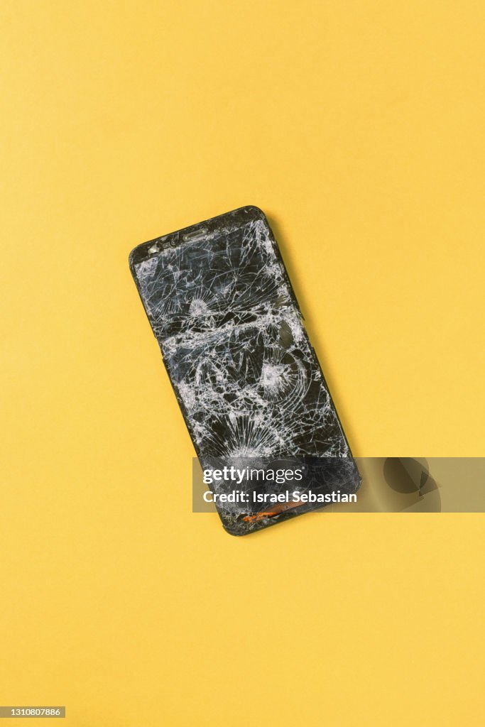 Top view of a broken cell phone on a yellow background.