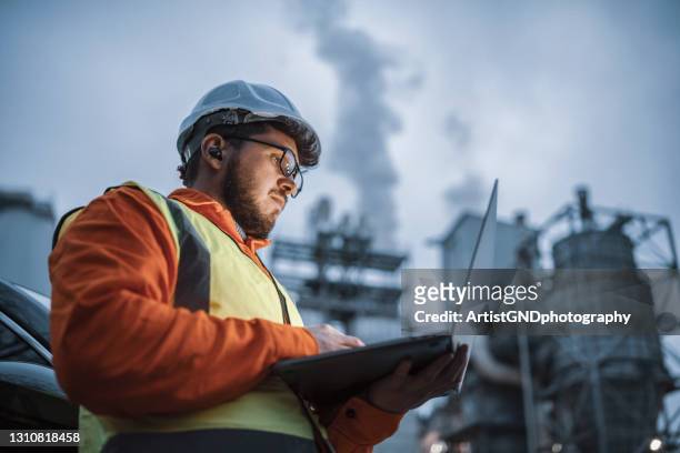 ingeniero serio y guapo usando un ordenador portátil mientras trabaja en la industria del petróleo y el gas. - factory fotografías e imágenes de stock