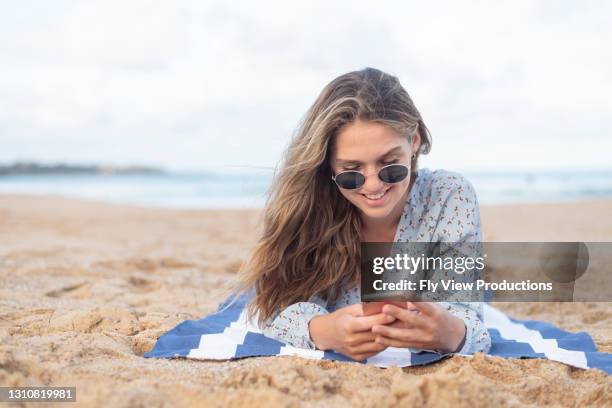 vrouw die mobiele telefoon terwijl bij het strand gebruikt - alleen jonge vrouwen stockfoto's en -beelden