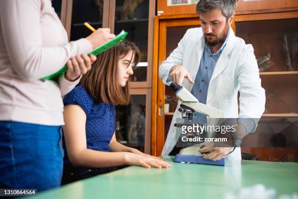 teacher giving instructions to high school girls for microscope use in biology class - surveillance society stock pictures, royalty-free photos & images