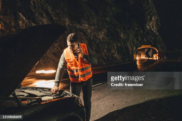 male driver in reflective waistcoat looking in car hood on roadside while talking with roadside service on phone - waistcoat isolated stock pictures, royalty-free photos & images