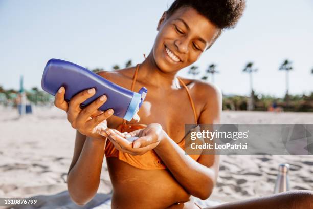 mulher tomando sol e aplicando loção bronzeada na praia - aplicando - fotografias e filmes do acervo