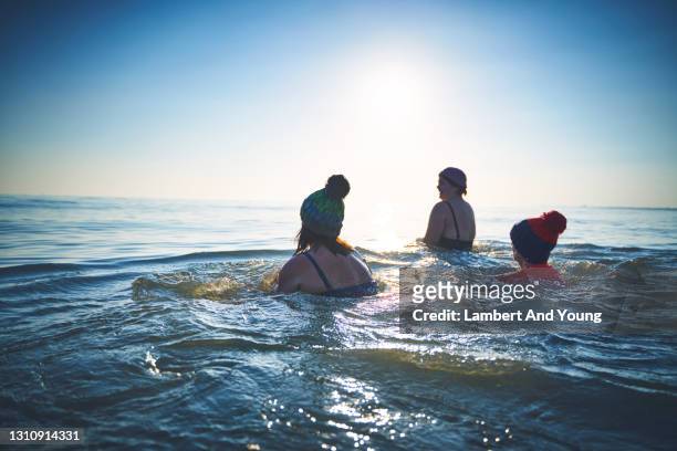 family winter sea swimming in wooly hats in bright sunlight - open water swimming stock pictures, royalty-free photos & images