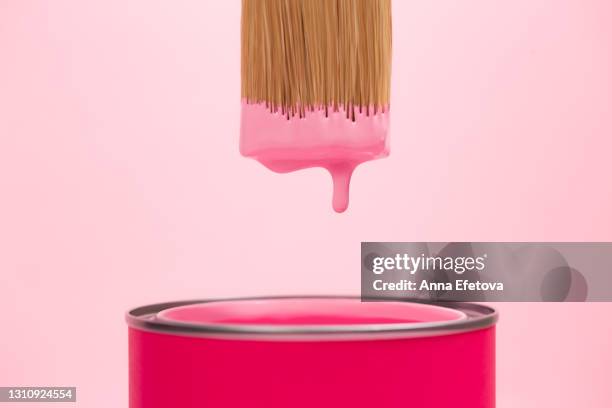 pink paint is dripping from paintbrush bristle into can with pigment against pastel pink background. concept of home repair. front view and close-up - ペンキ缶 ストックフォトと画像