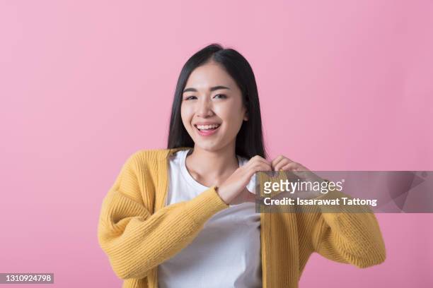 pretty romantic young woman making a heart gesture with her fingers in front of her chest showing her love and affection with a happy tender smile - young at heart ストックフォトと画像