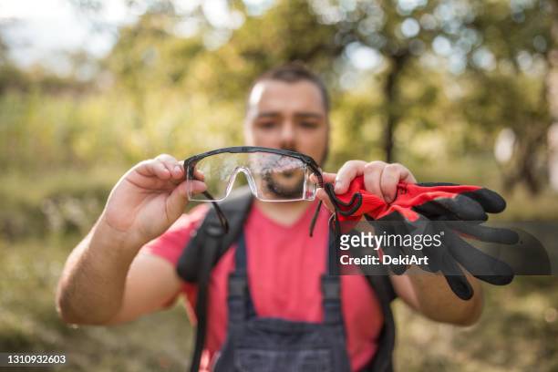 fermier retenant des lunettes protectrices et des gants coupant l’herbe dans l’arrière-cour - agriculture stock photos et images de collection