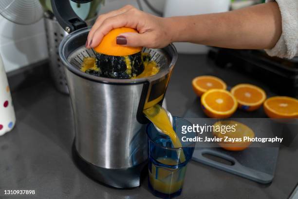 woman making fresh squeezed orange juice using an electric squeezer - saftpresse stock-fotos und bilder