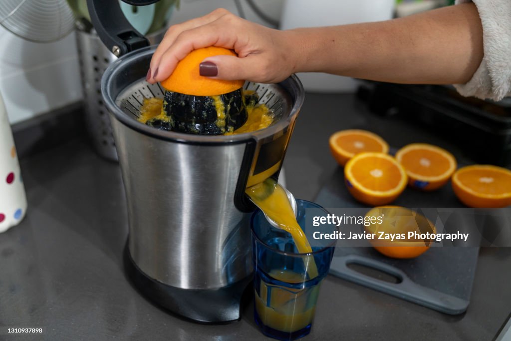 Woman Making Fresh Squeezed Orange Juice Using An Electric Squeezer