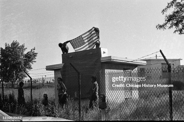 Native Americans stand on top of a building holding an American flag during their occupation of the Nike site at Belmont Harbor, Chicago, Illinois,...