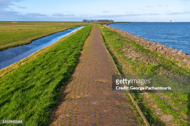 walking path on top of a levee next to the sea - polder barrage photos et images de collection