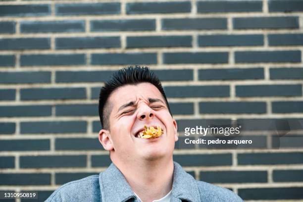 young man with a lot of chips in his mouth laughing - südeuropa stock-fotos und bilder