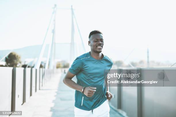 modern african male running on bridge and enjoying music - black alley stock pictures, royalty-free photos & images