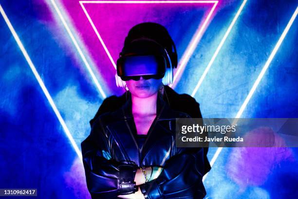 portrait of young confident woman standing against projection screen, arms crossed. she is lighted with colorful neon triangles. - casques réalité virtuelle photos et images de collection