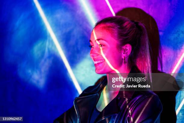 close-up portrait of young woman standing against projection screen and smiling. she is lighted with pink and blue neon colours - panel gaming art or commerce stockfoto's en -beelden