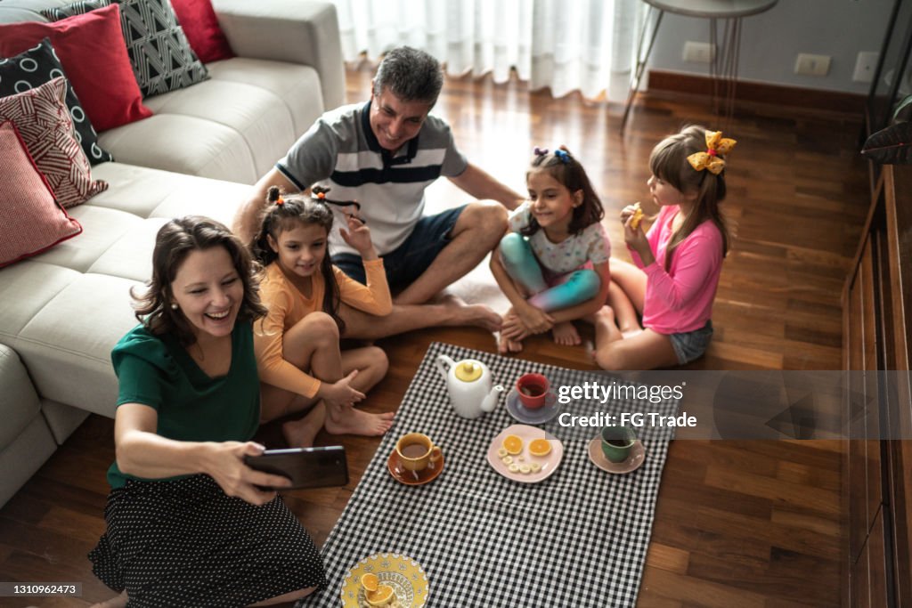 Family doing a video call on mobile phone during indoors picnic at home