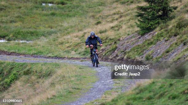 single caucasian male biker riding downhill on a mountain path - wandelen stock pictures, royalty-free photos & images