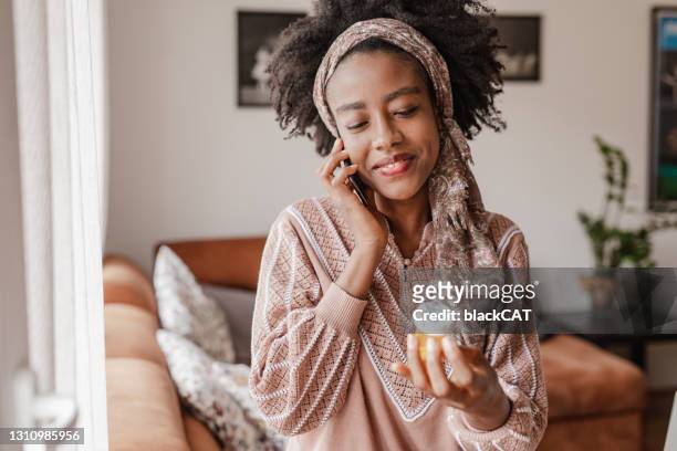 african american woman calls health services over the phone and seeks medical advice while holding a bottle of pills in her hand - prescription medicine stock pictures, royalty-free photos & images