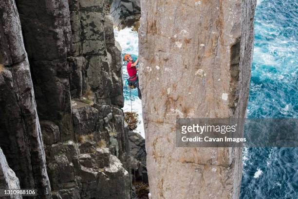 adventurous man rockclimbs an exposed rock column with sea cliffs and the ocean in the background in the totem pole, cape hauy, tasman national park, tasmania, australia. - totem pole stock pictures, royalty-free photos & images