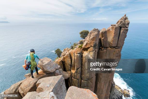 female adventurer heads off into the unkown, armed with ropes and climbing gear, as she explores dolerite rock columns in the  sea cliffs of cape raoul, in tasmania, australia. - hiking tasmania stock-fotos und bilder