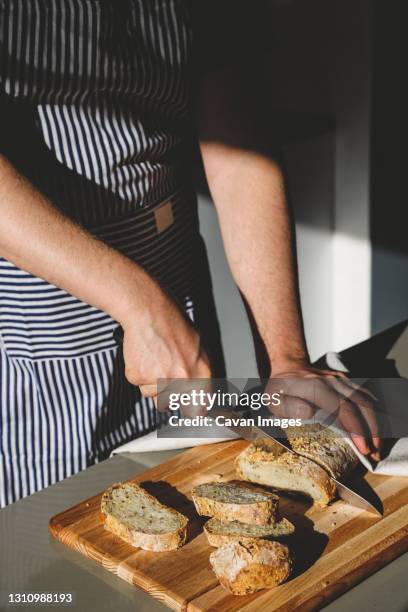 a man cuts bread on a wooden board - scoring bread stock pictures, royalty-free photos & images