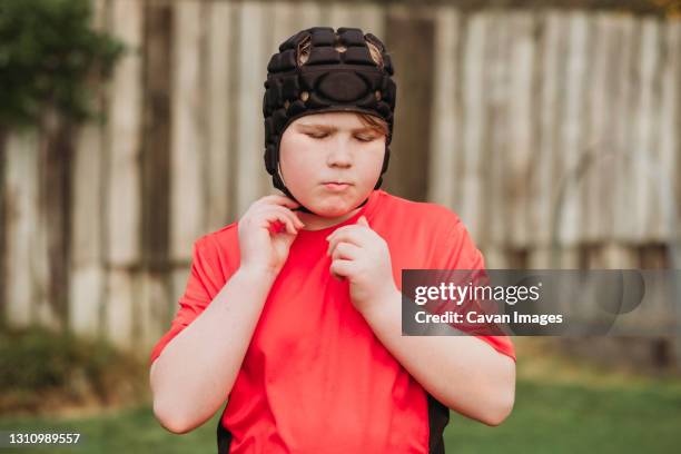 boy putting on rugby protection head gear in backyard - liga de rugby fotografías e imágenes de stock