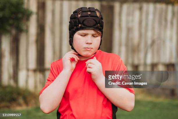 boy putting on rugby protection head gear in backyard - rugby league stockfoto's en -beelden