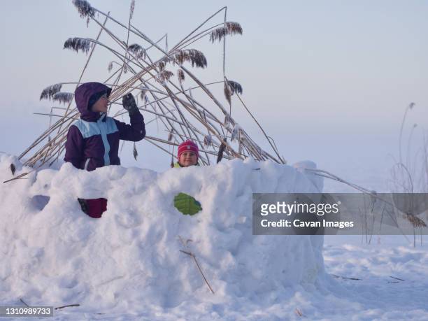 girls playing in snow fortress on frozen lake during cold winter day - kids fort stock pictures, royalty-free photos & images