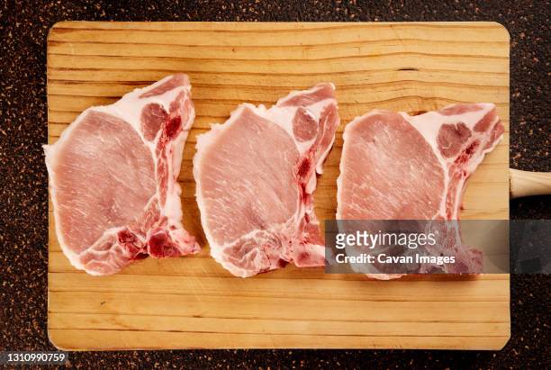 top view of three raw pork chops on a wooden cutting board - pork bildbanksfoton och bilder
